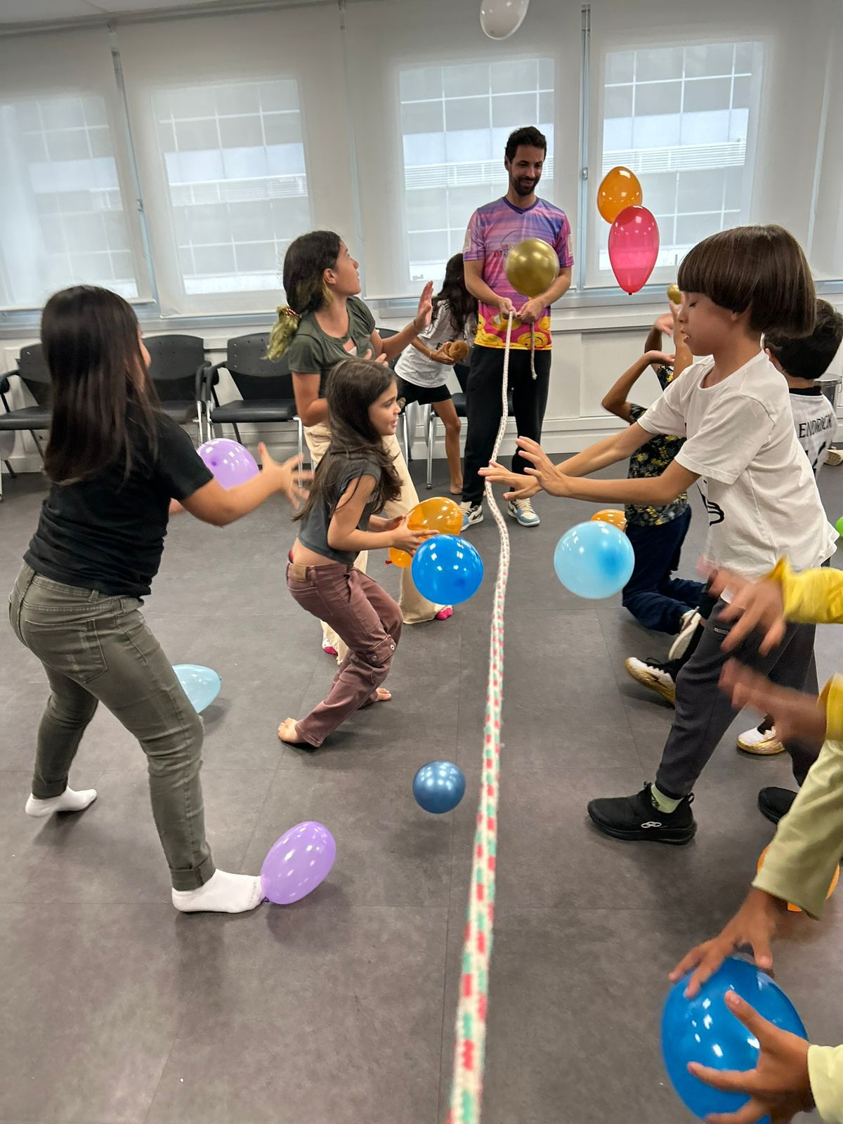 Crianças brincando com balões, tentando passar o máximo de balões no campo adversário, separados por uma corda