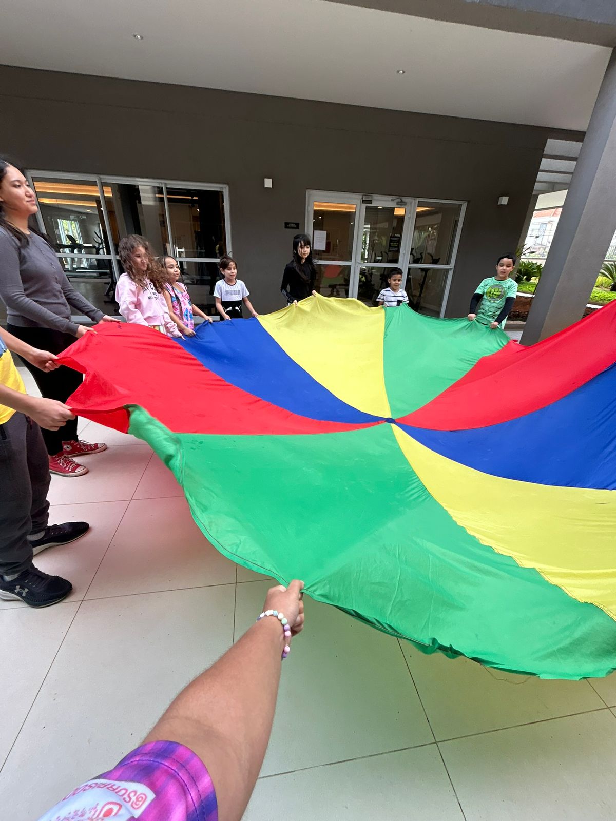 Uma grande brincadeira com um pano colorido gigante, sendo segurado por várias crianças de várias idades